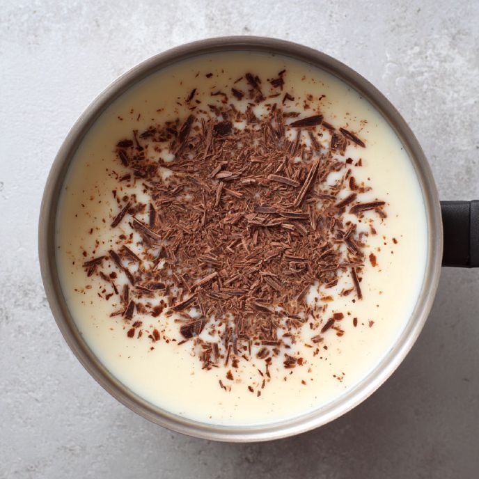 Warm milk and cream in a pot with shaved chocolate, top view