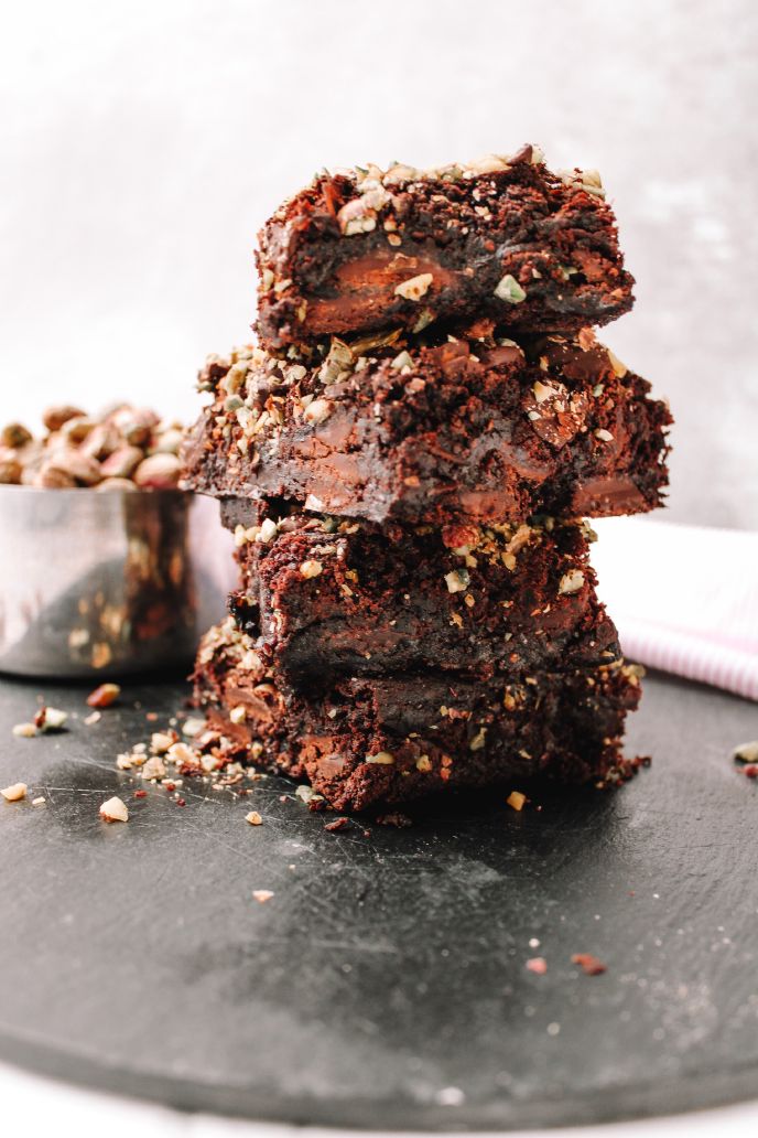 Fudgy pumpkin brownies stacked on a tray with chopped nuts